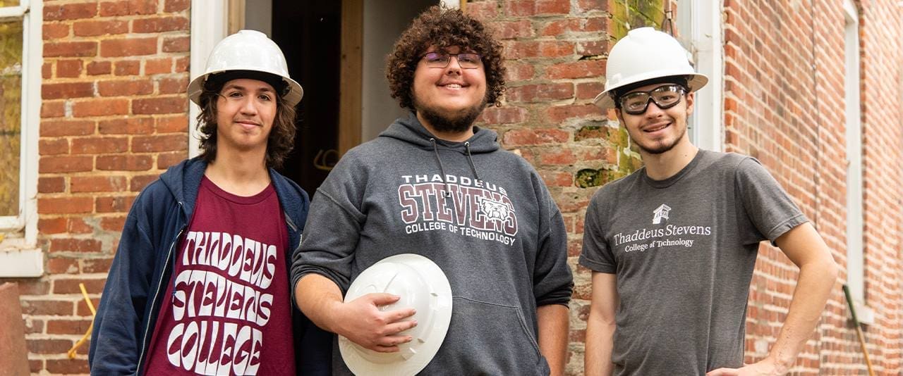 Three students wearing hard hats and Stevens gear smiling at camera. 