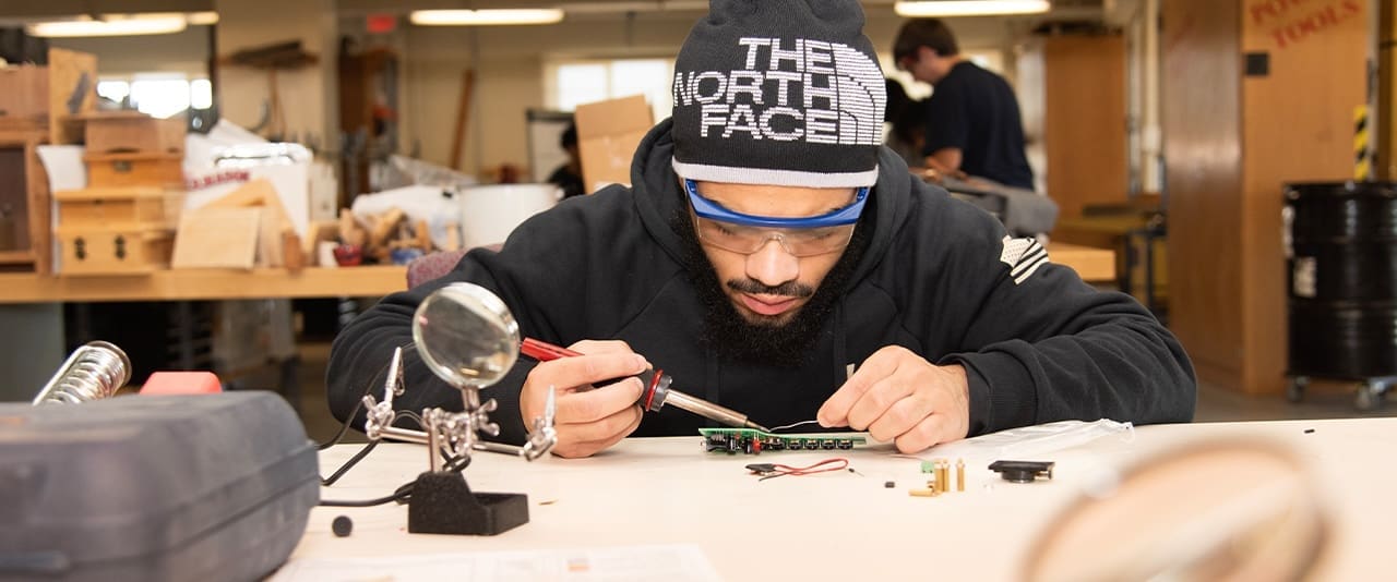 Thaddeus Stevens College student wearing safety glasses and a North Face beanie holding tool in lab