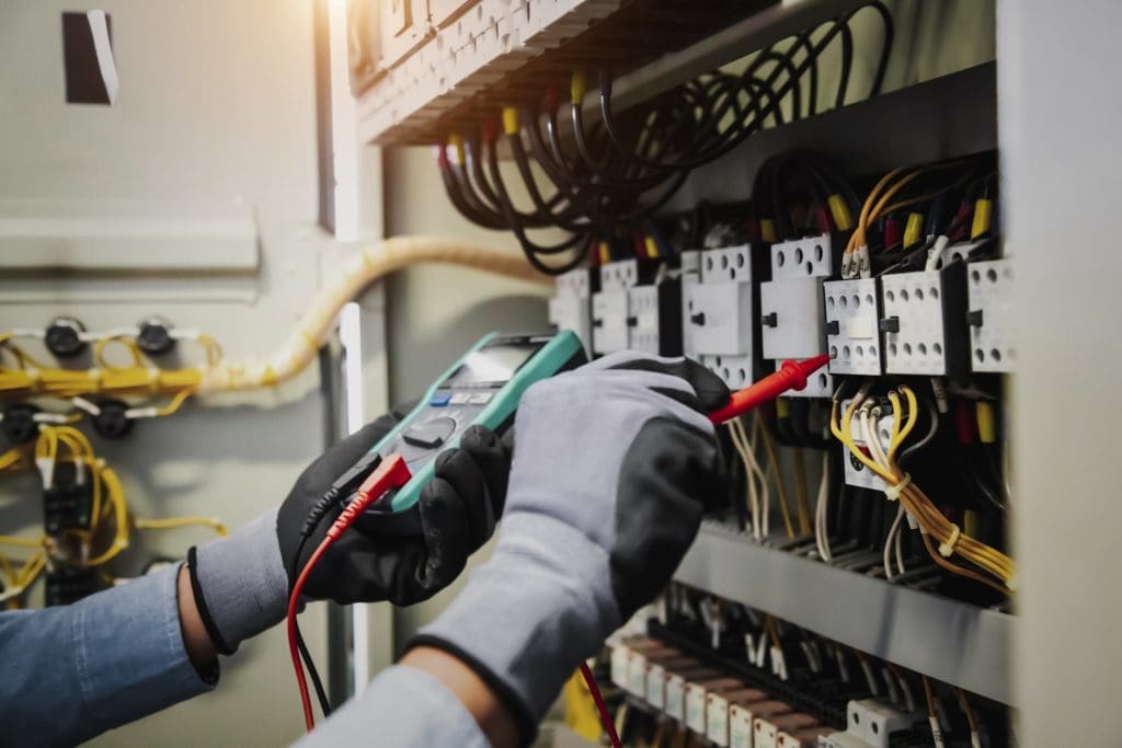 Hands with gloves fixing electrical wiring in box while testing wires in the other hand