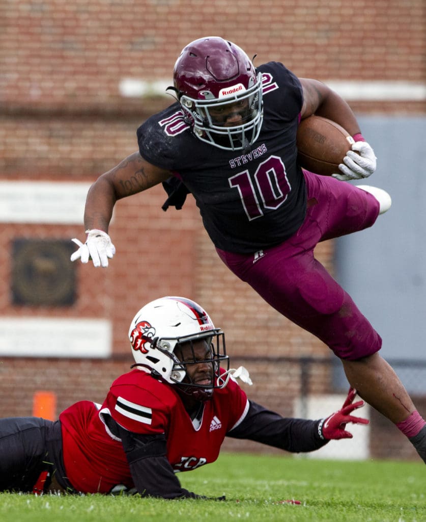 A football player jumps over a member of the opposing team during a game. 