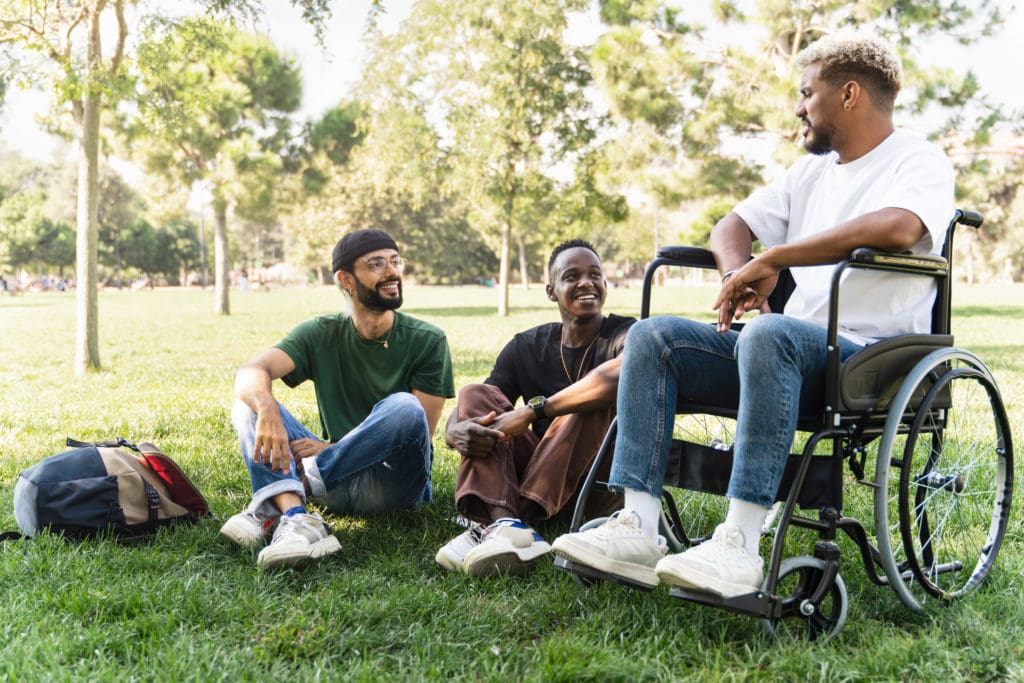 Two young men sitting on the college lawn next to their peer in a wheelchair