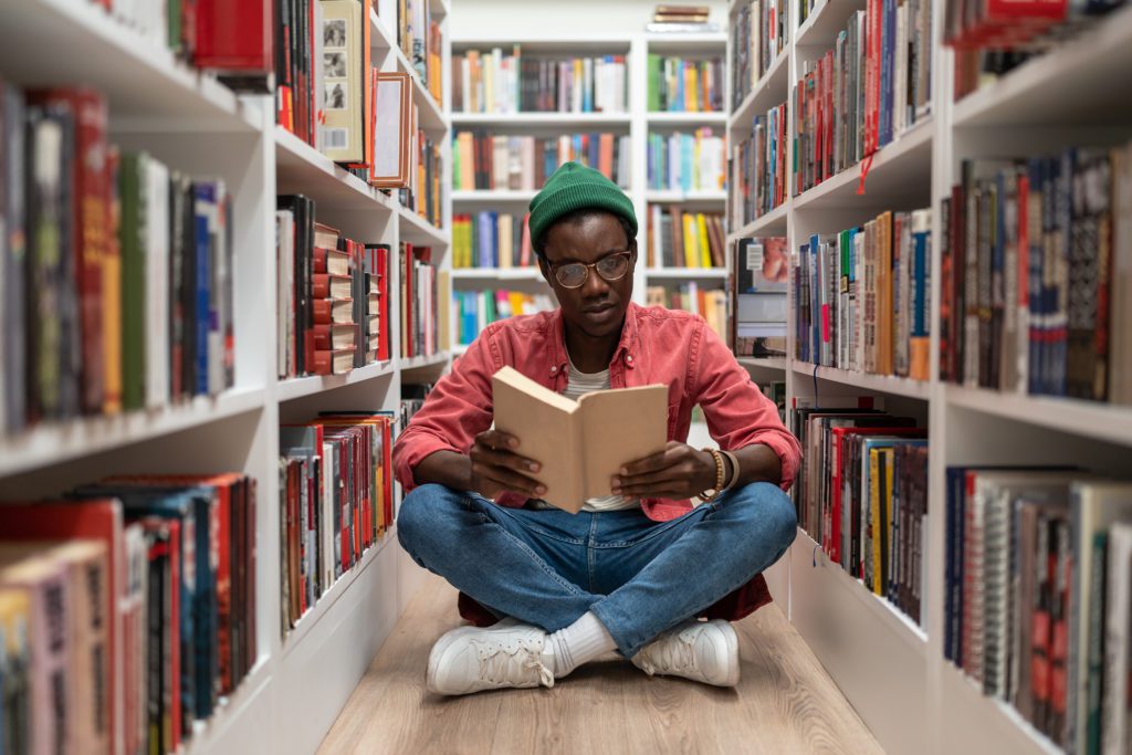 Student sitting on the floor reading in the library. 