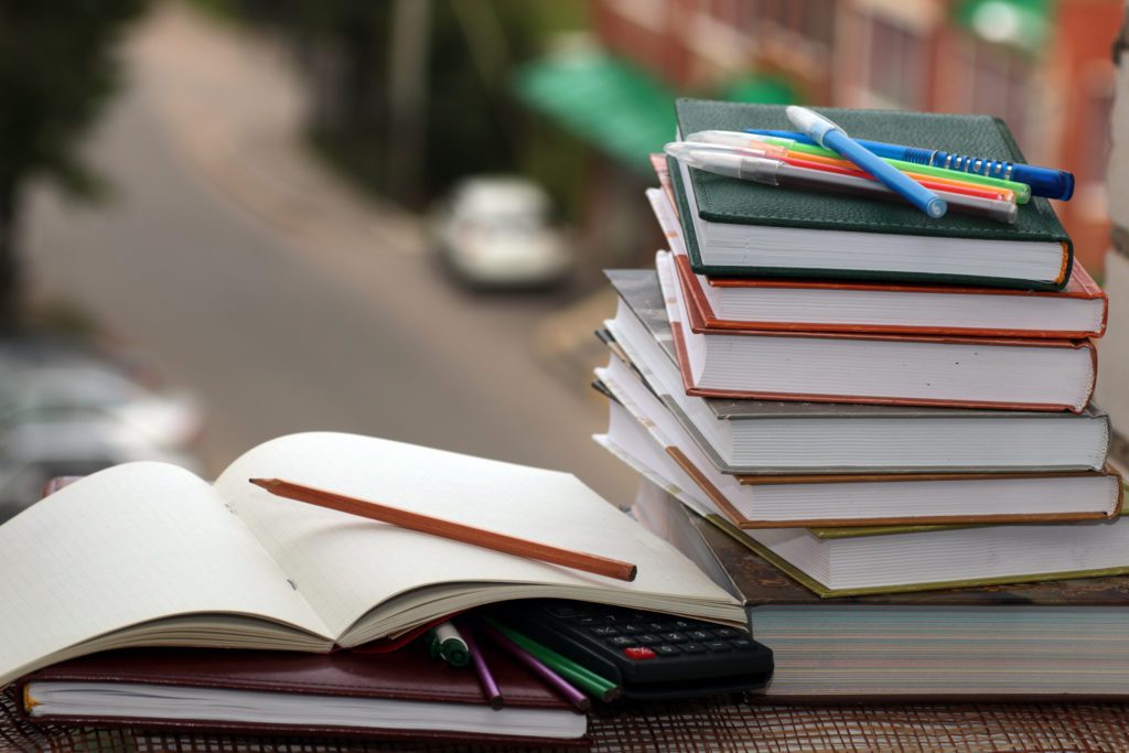 textbooks for studying stacked on a table, one open with a pencil on it.